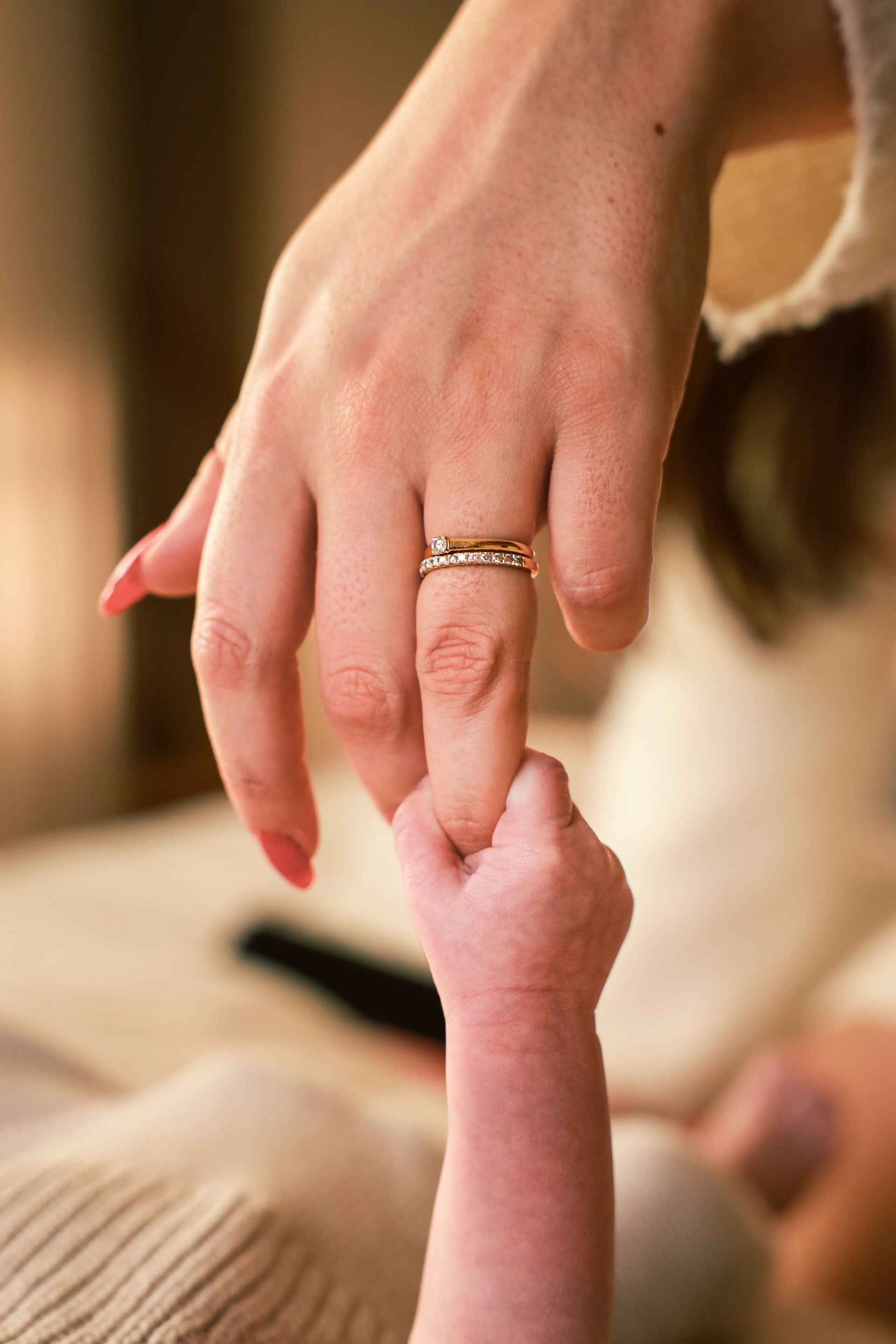 Een volwassen hand die de vinger van een baby vasthoudt, close-up in warm binnenlicht. Studio fotoshoot newborn.