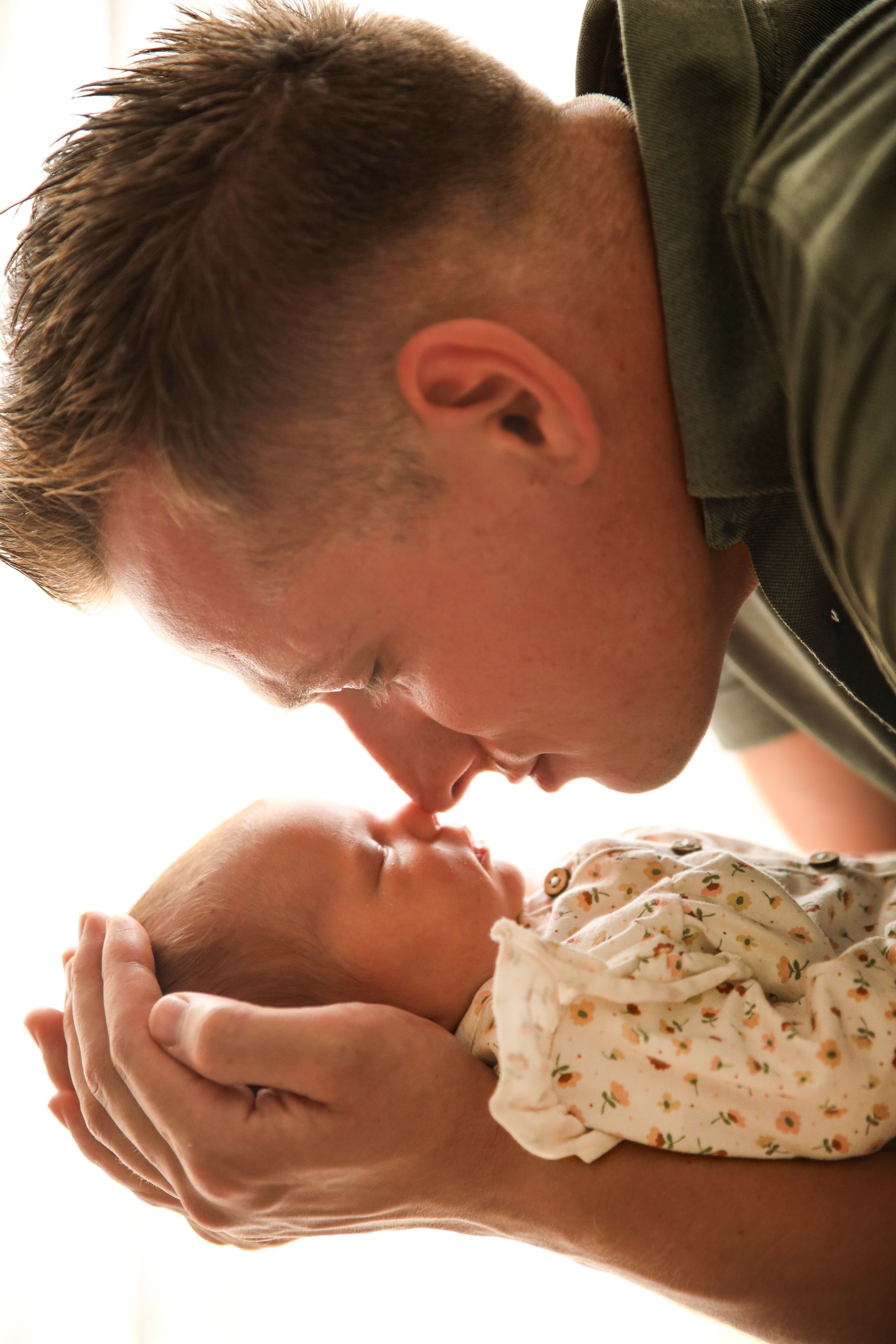 Een man kust teder een pasgeboren baby op het voorhoofd; vader en baby. Newborn fotoshoot met ouders. 