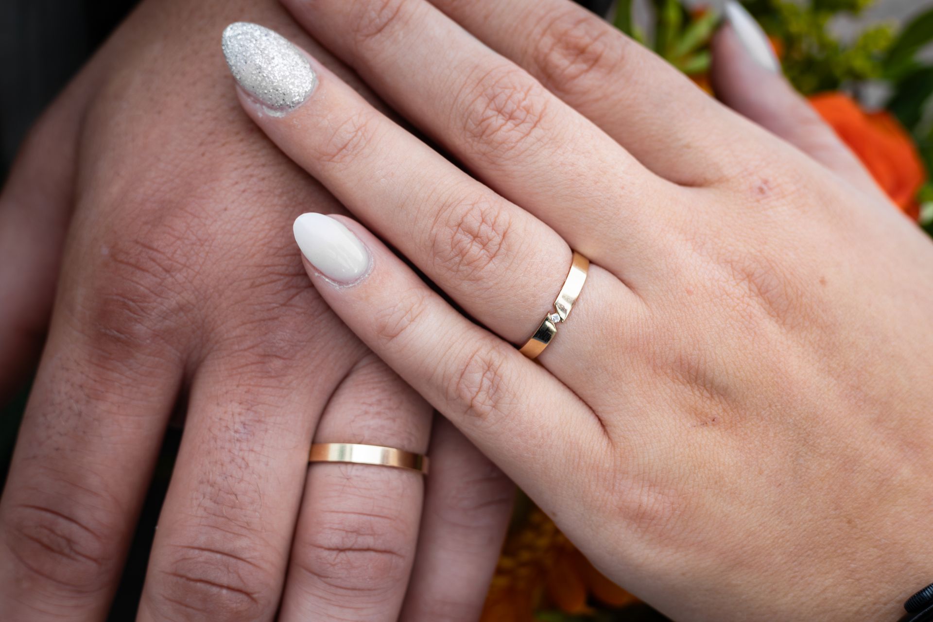 Twee handen met bijpassende gouden ringen en wit gemanicuurde nagels, die buiten naast elkaar rusten.