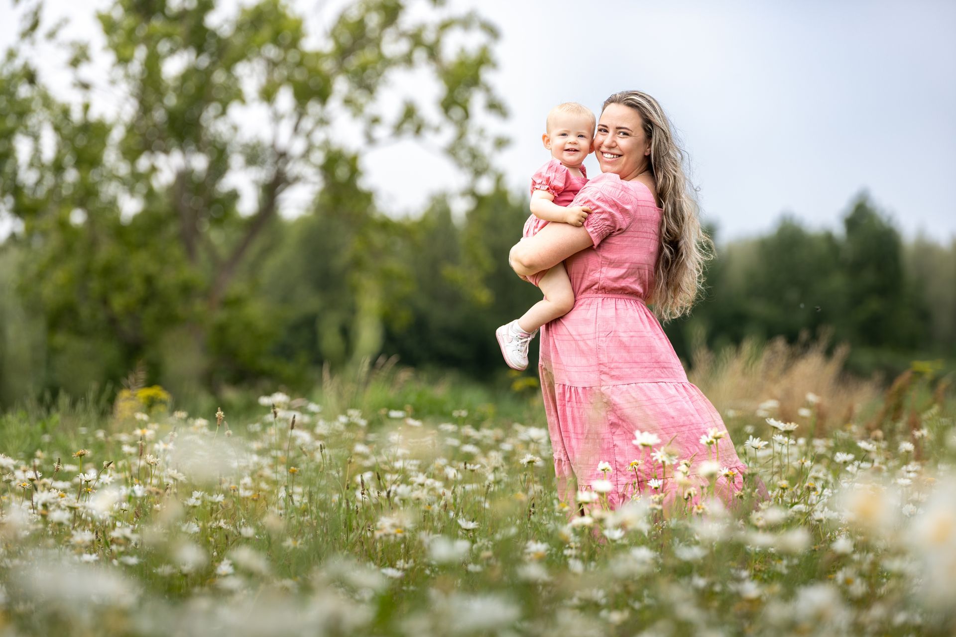 Vrouw in een roze jurk met een peuter in een bloemenweide in de buitenlucht Moeder dochter fotoshoot. Moeder dochter shoot.