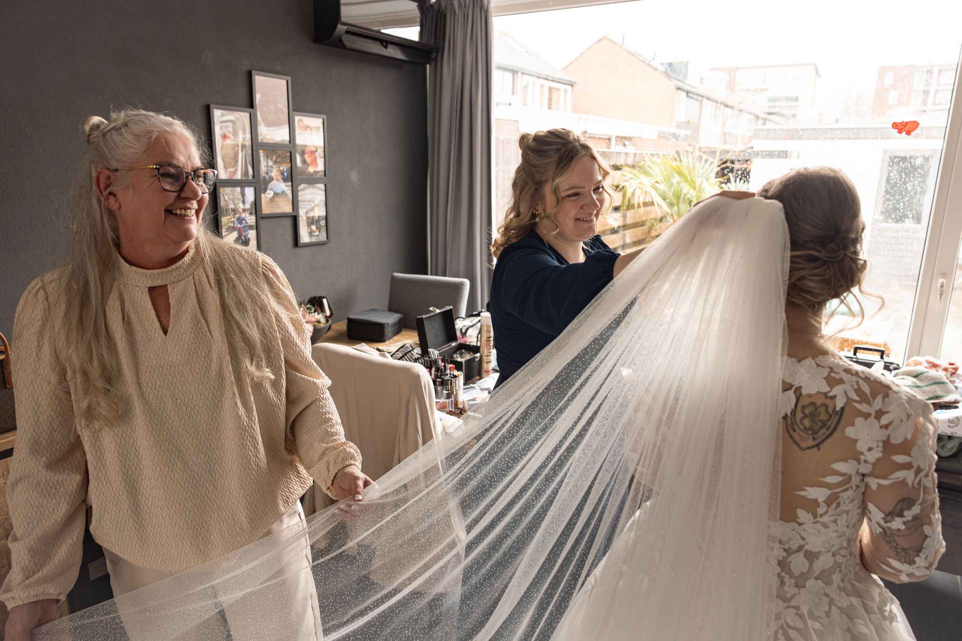 Een bruid krijgt een lange witte sluier aan door familie. Bruidsfotografie Voorne Putten. Bruidsfotograaf Voorne aan Zee.