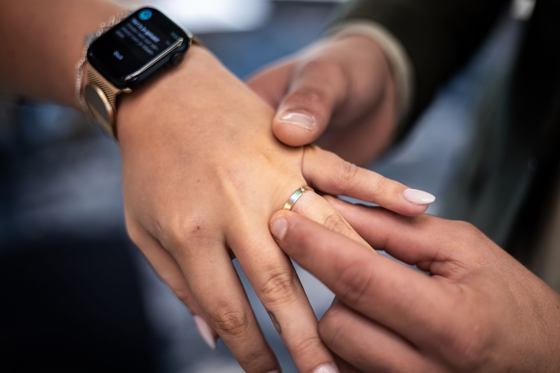 Twee handen die elkaar vasthouden, één hand draagt een smartwatch en een trouwring, close-up binnen. Trouwfotograaf.