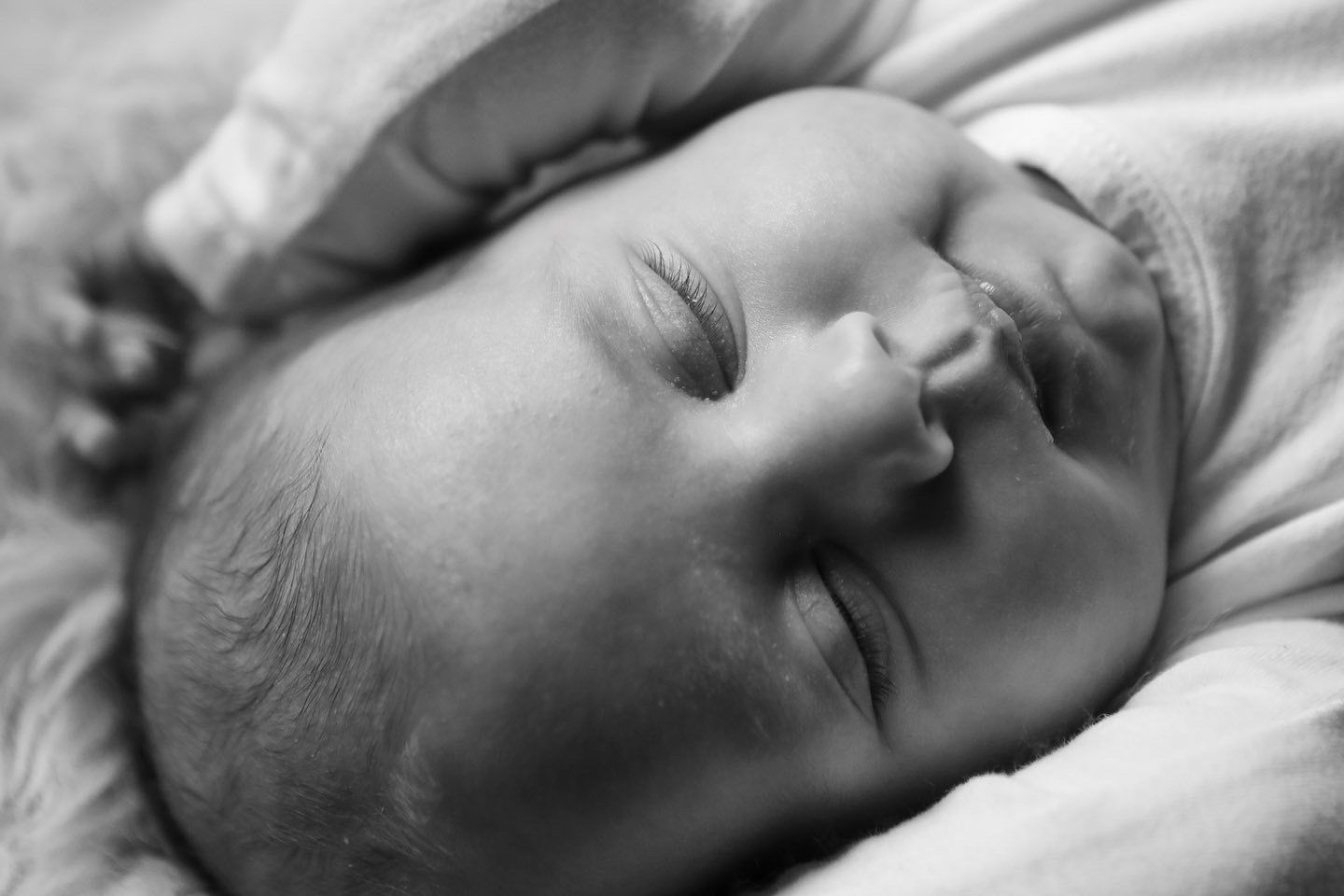 Een slapende pasgeborene ligt op een zachte deken, met gesloten ogen. Lifestyle newborn fotograaf Hellevoetsluis.