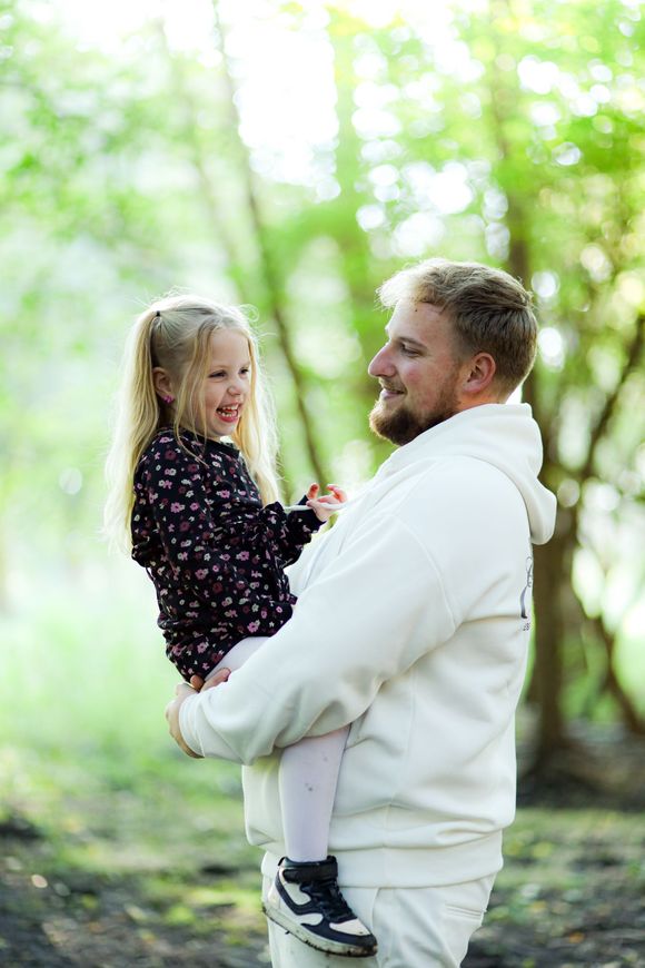Man die een lachend kind vasthoudt in een heldere, groene buitenomgeving. Vader dochter fotoshoot. Goedkope Gezinsfoto's.