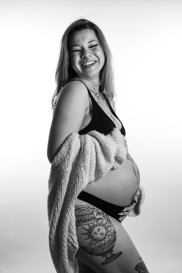 Een glimlachende zwangere vrouw, staand in profiel tegen een witte achtergrond. Zwangerschap fotoshoot goedkoop.