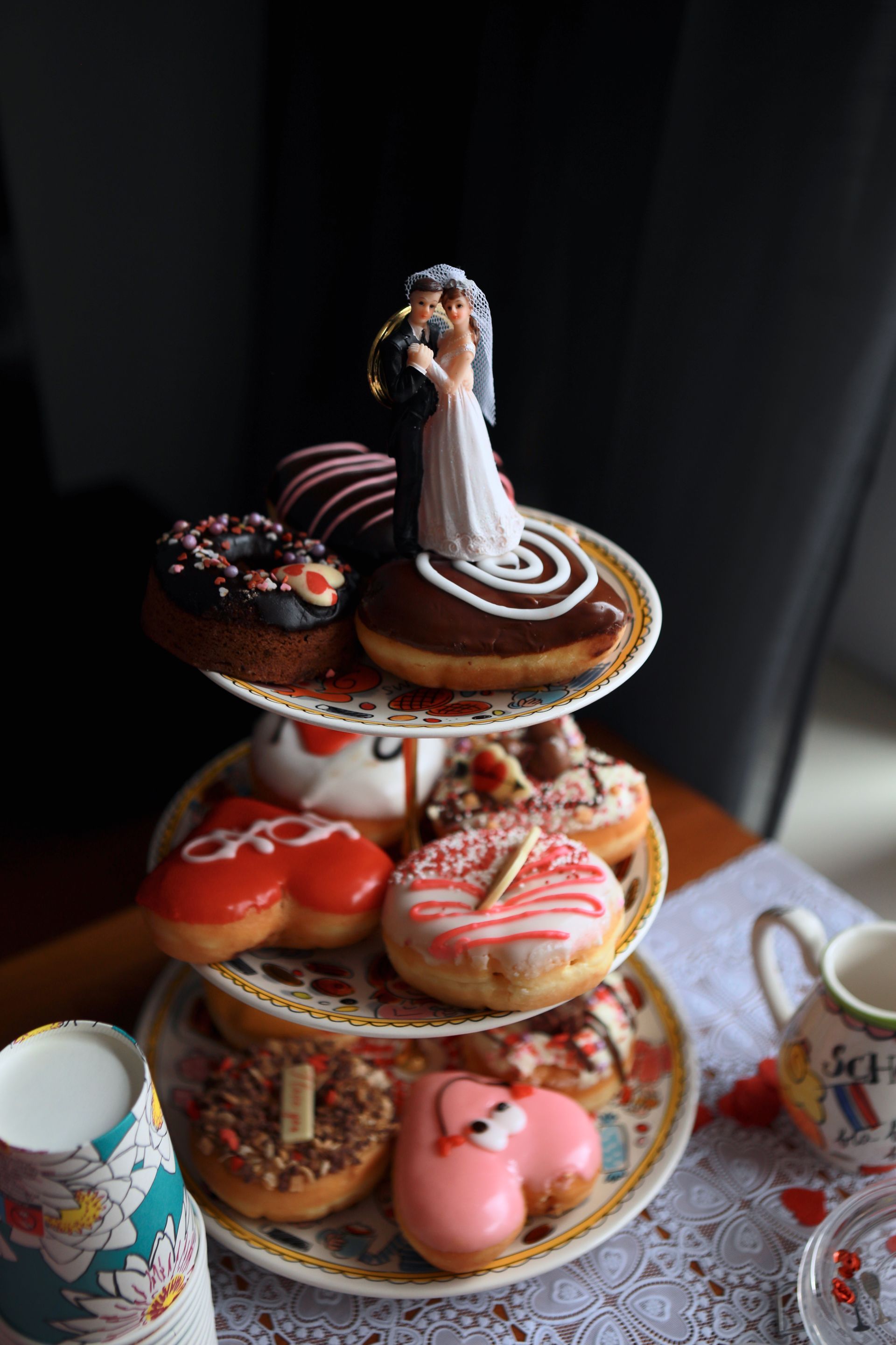 Versierde etagère met diverse donuts en een bruidje als decoratie op een tafel.