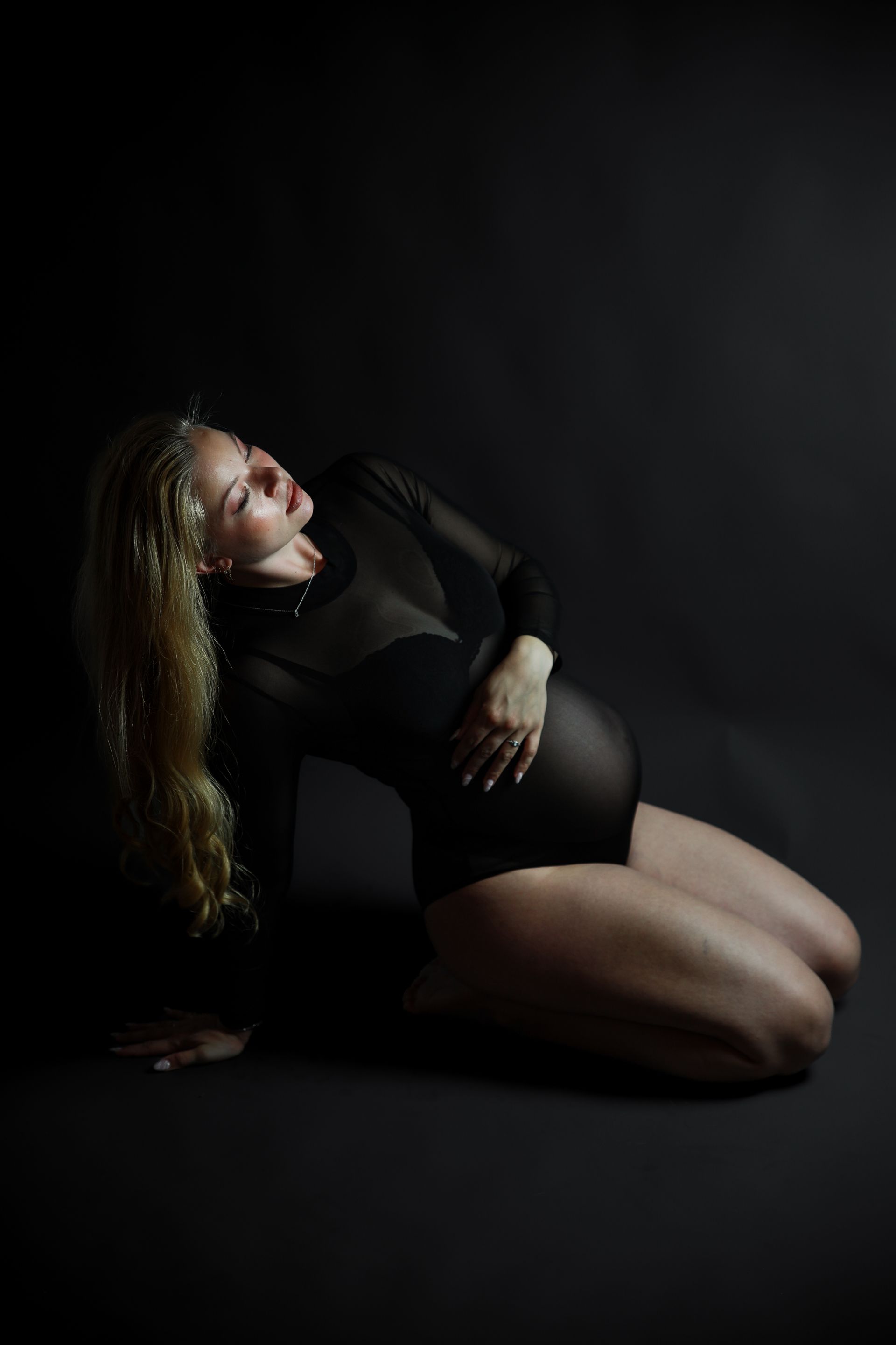 Een zwangere vrouw in een zwarte outfit ligt achterover , met haar hand op haar buik. Zwanger fotoshoot.