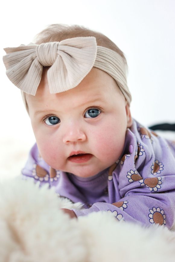 De baby, gewikkeld in een paarse deken met een beige strik in haar haar, kijkt naar de camera. Kinderfotoshoot.