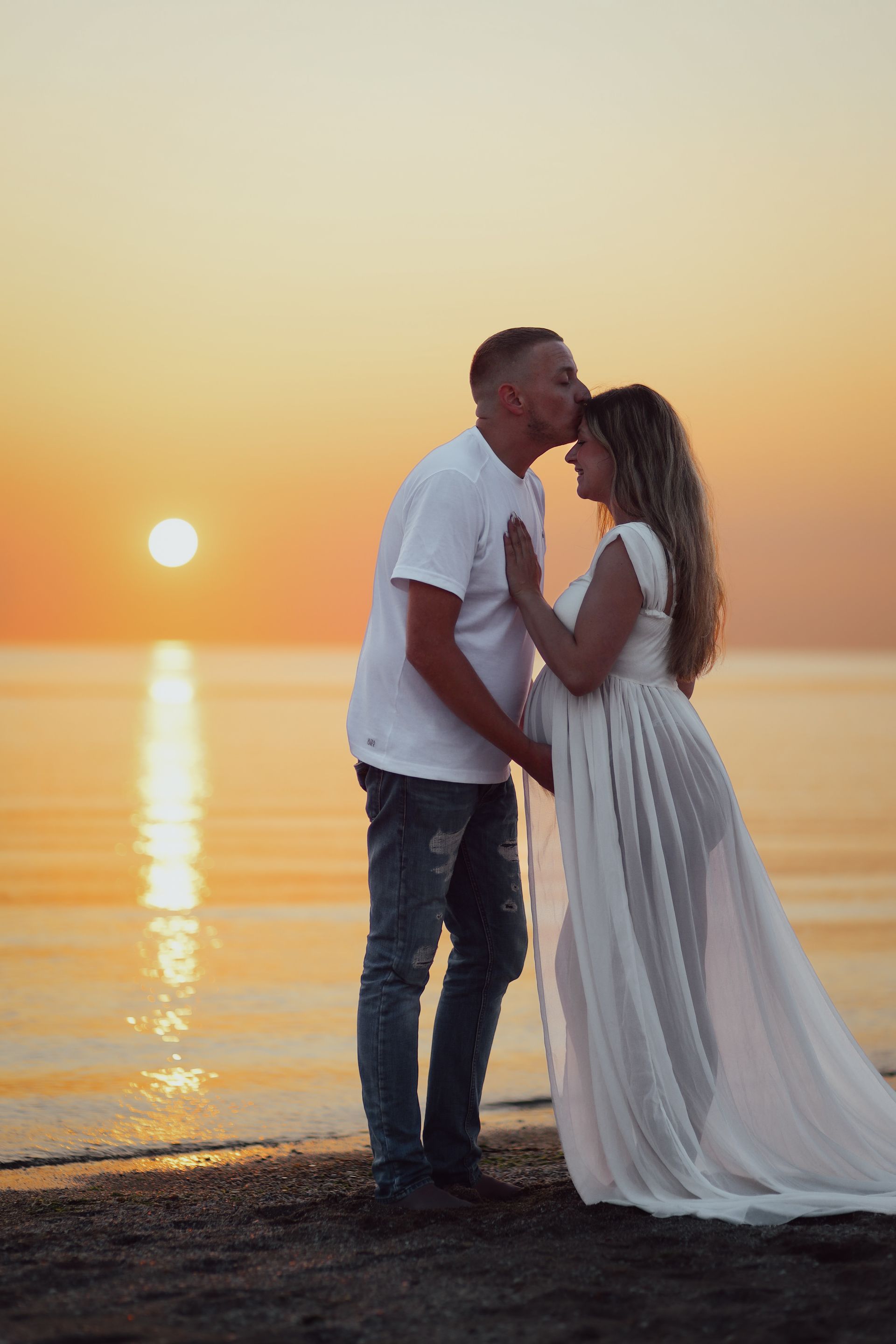 Een stelletje dat elkaar kust bij zonsondergang op het strand. Zwangerschapsfotografie. Zwangerschapspakket. Newbornpakket.