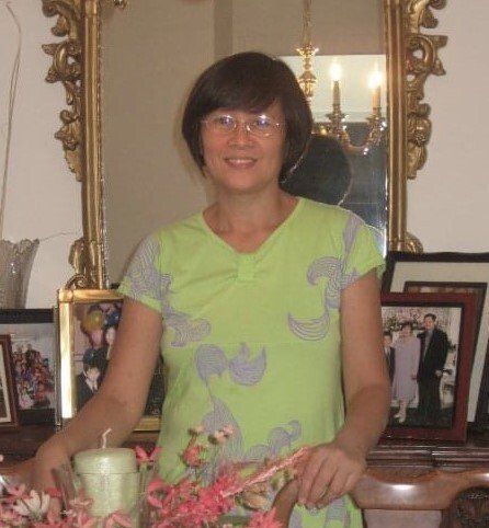 Woman in green dress, smiling, near a mirror and framed photos, indoors.