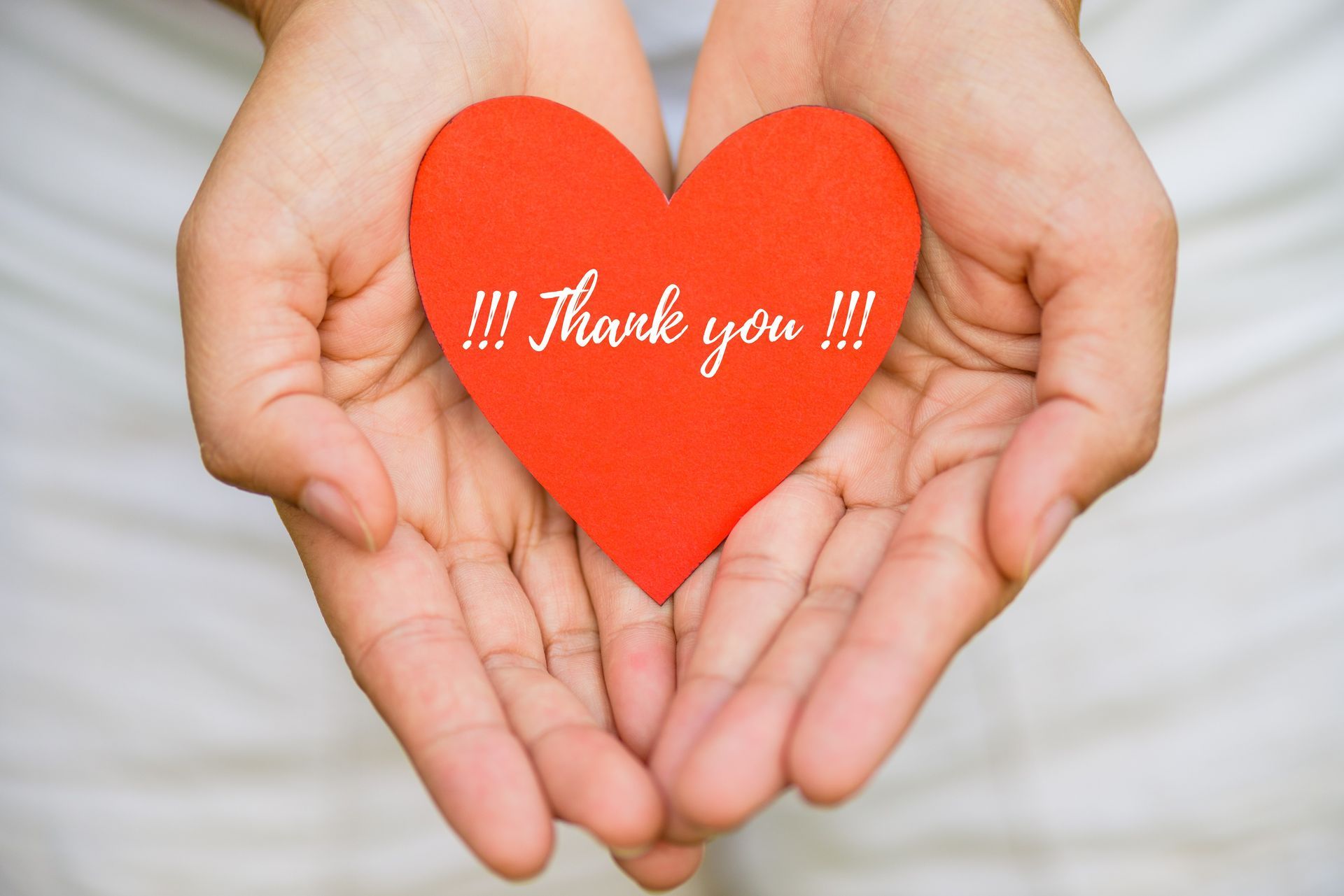 Hands cupped, holding a red heart-shaped card with “Thank you !!!” written on it.