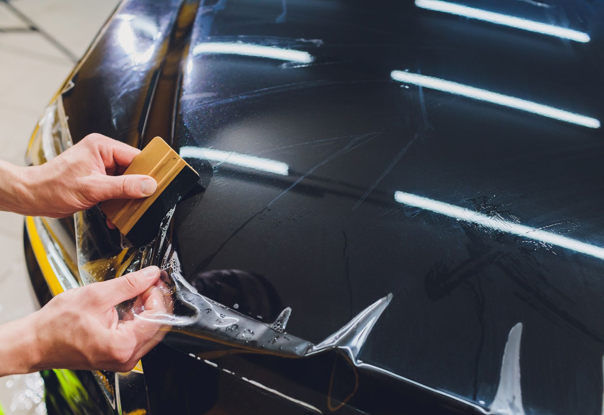PPF installation on a black car hood.