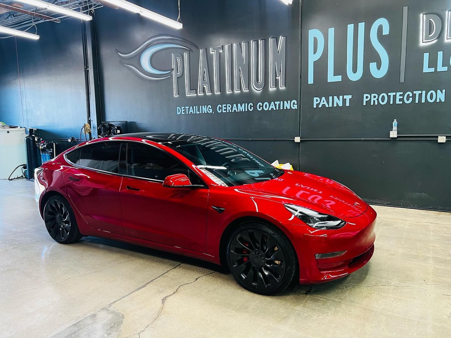 Red Tesla with window tint inside Platinum Plus Detailing shop for ceramic coating and paint protect
