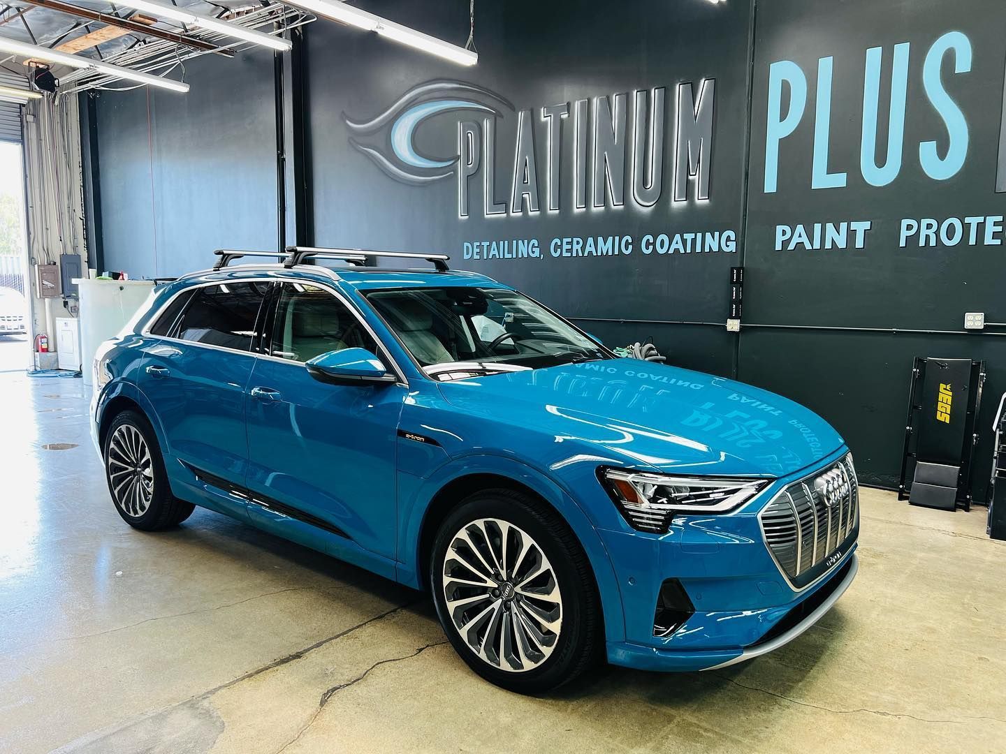 Blue Rivian electric pickup truck parked indoors, flags in background.