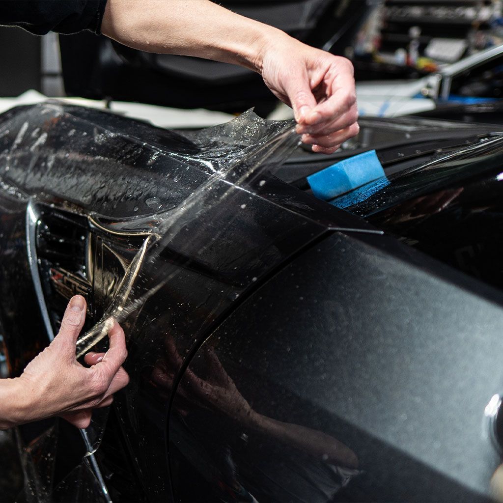 A person is wrapping a car with plastic wrap.