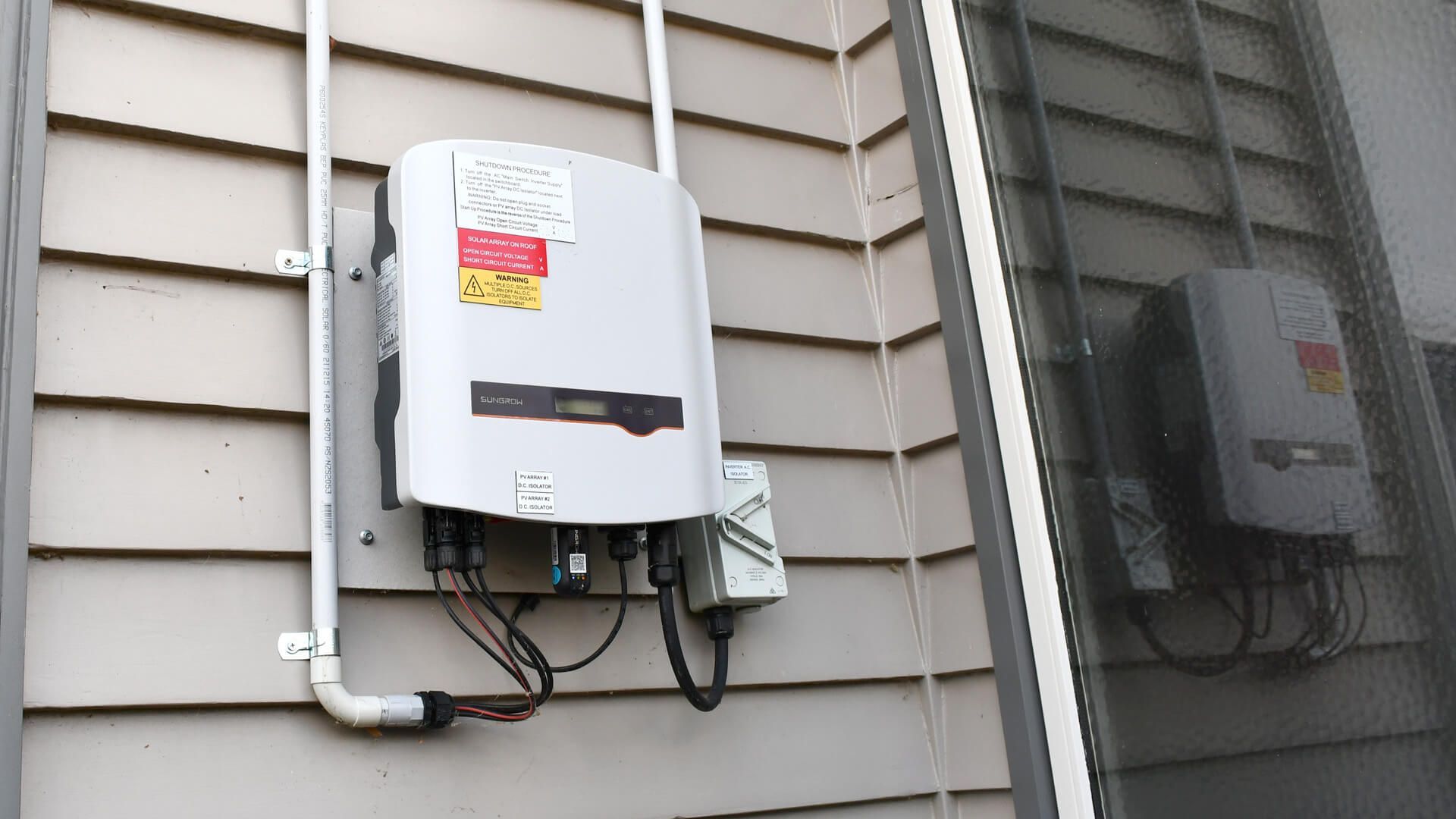 A leading brand solar inverter is attached to the side of a house.