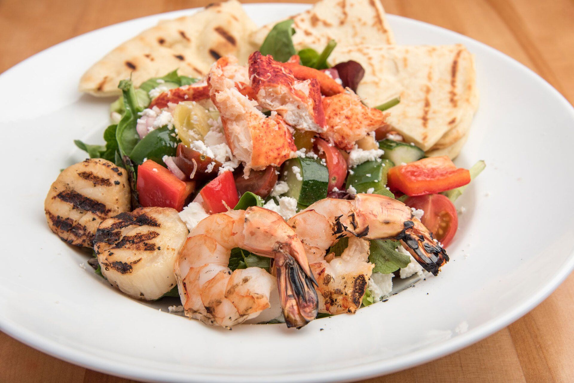 A white plate topped with a salad of shrimp , scallops , tomatoes and pita bread.