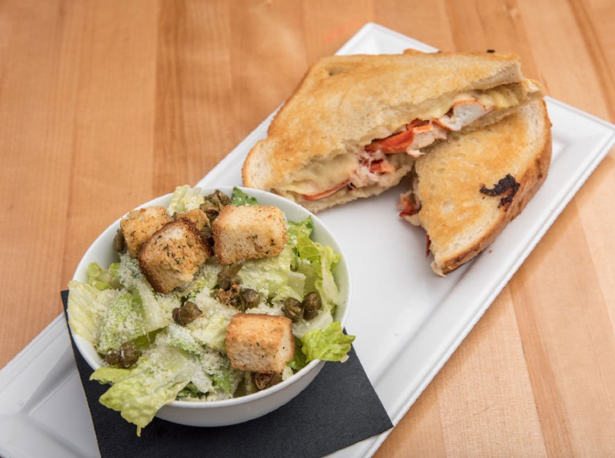 A sandwich and a bowl of salad are on a white plate.