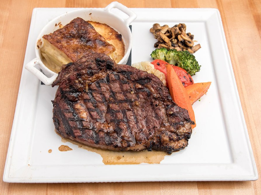 A white plate topped with a steak and vegetables on a wooden table.