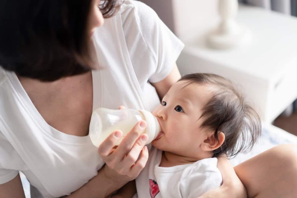 A person in a white shirt holding a baby and feeding them with a bottle.