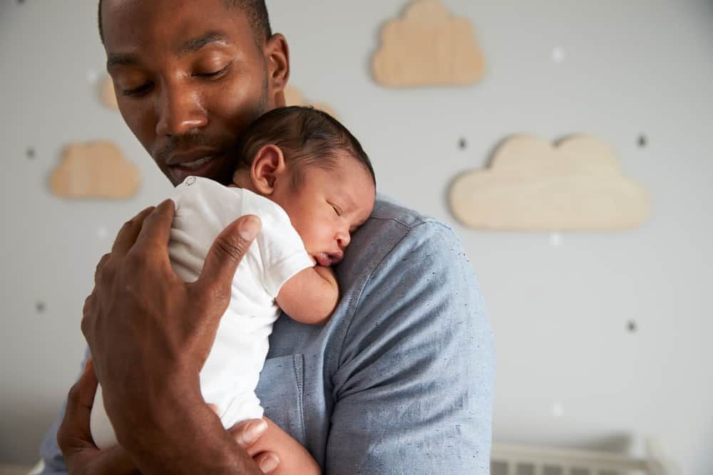 A person in a blue shirt holds a sleeping newborn against their shoulder in a room decorated with wall cloud cutouts.