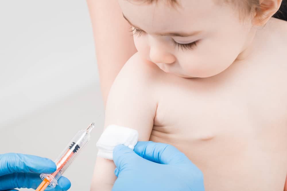 A healthcare provider in blue gloves prepares to give an injection to a patient's arm.