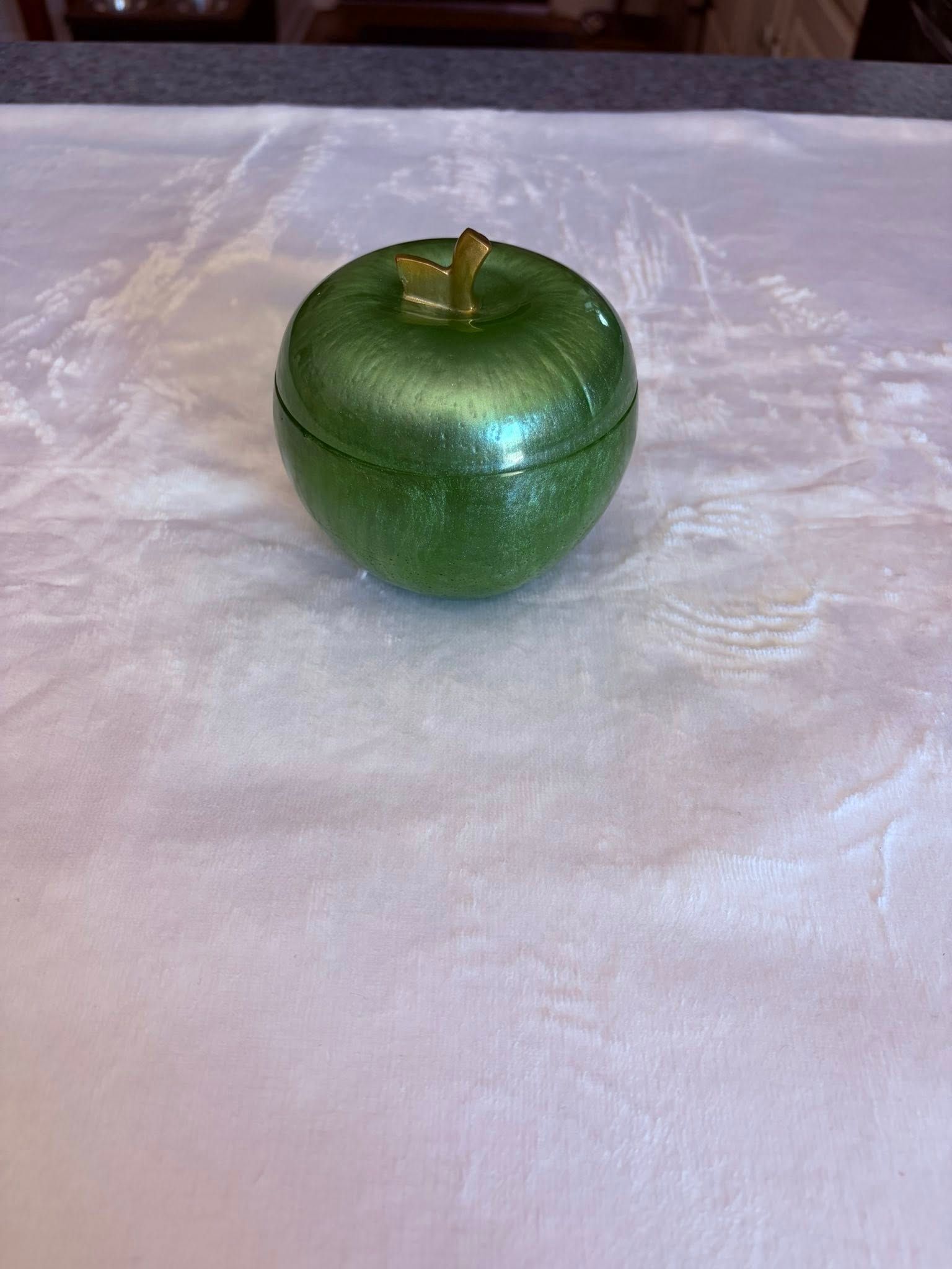 Green textured decorative apple-shaped container with a gold stem on a white cloth surface