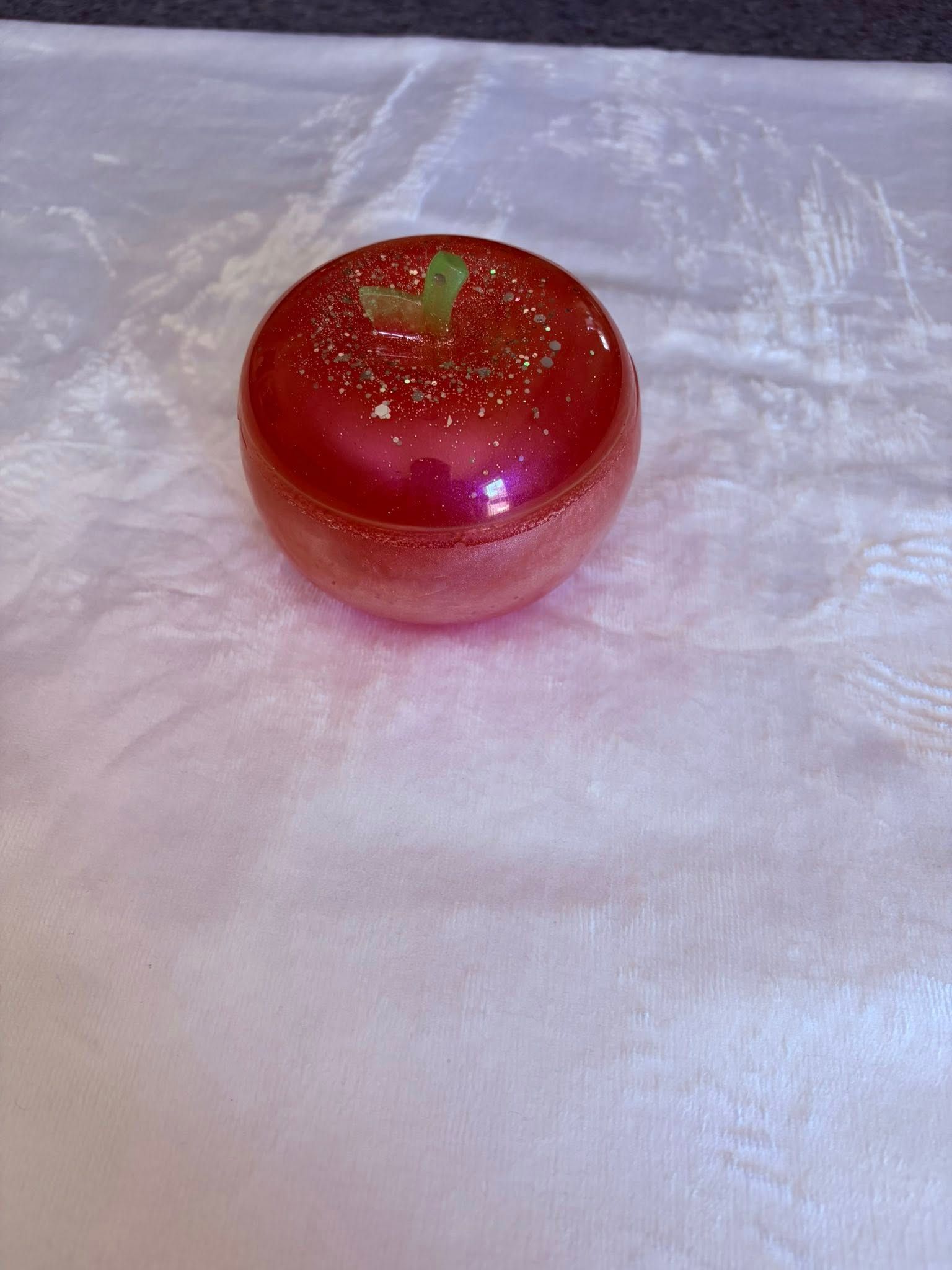Red glittery round container with a clear lid on a white fabric surface.