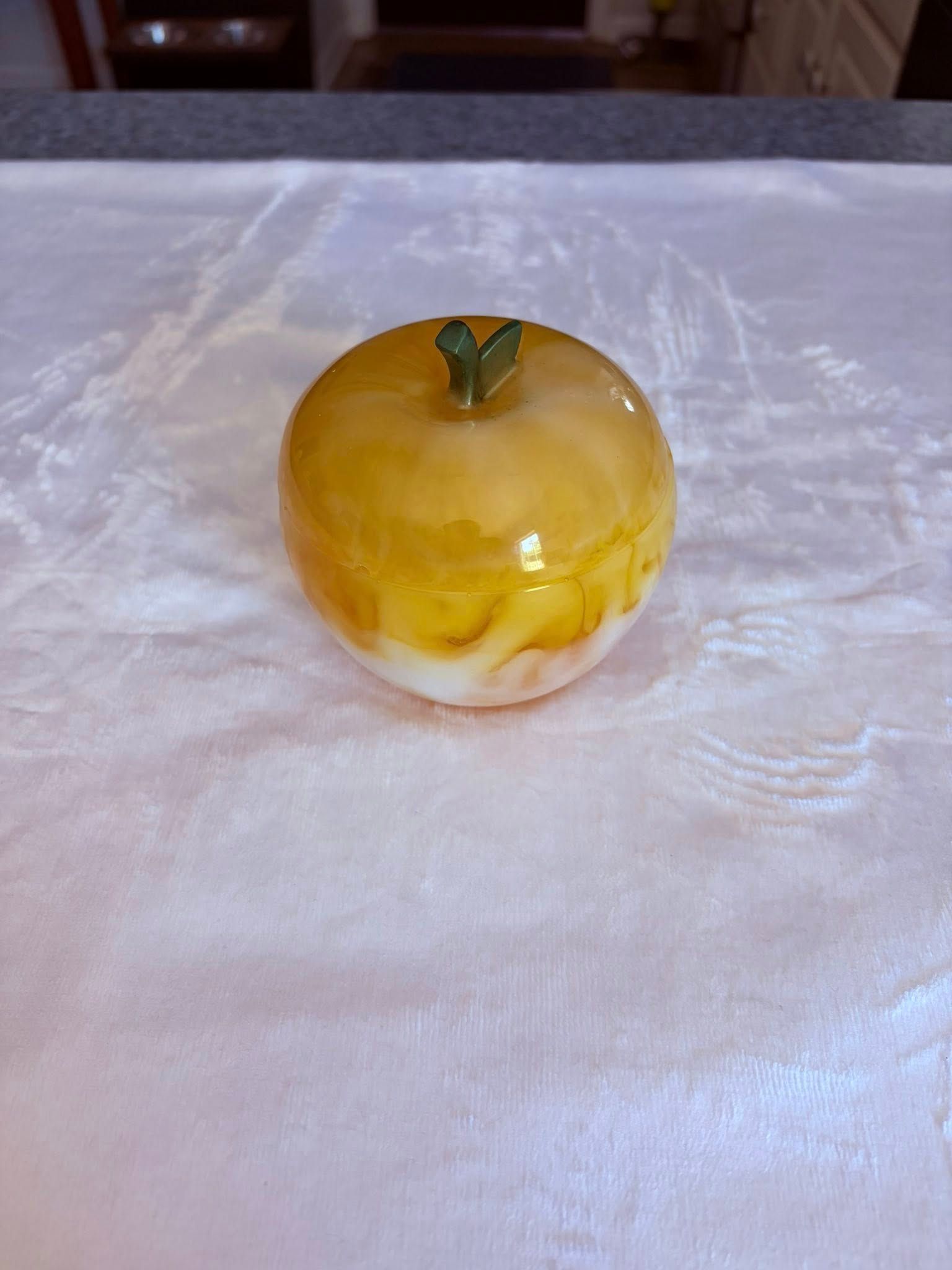 Yellow glass apple ornament with a green leaf, resting on a white cloth