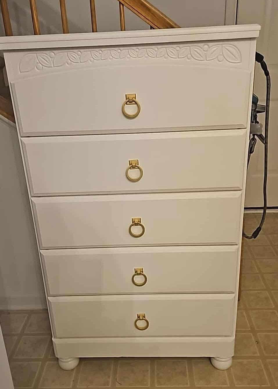 White five-drawer dresser with gold ring pulls in a room, slightly angled view