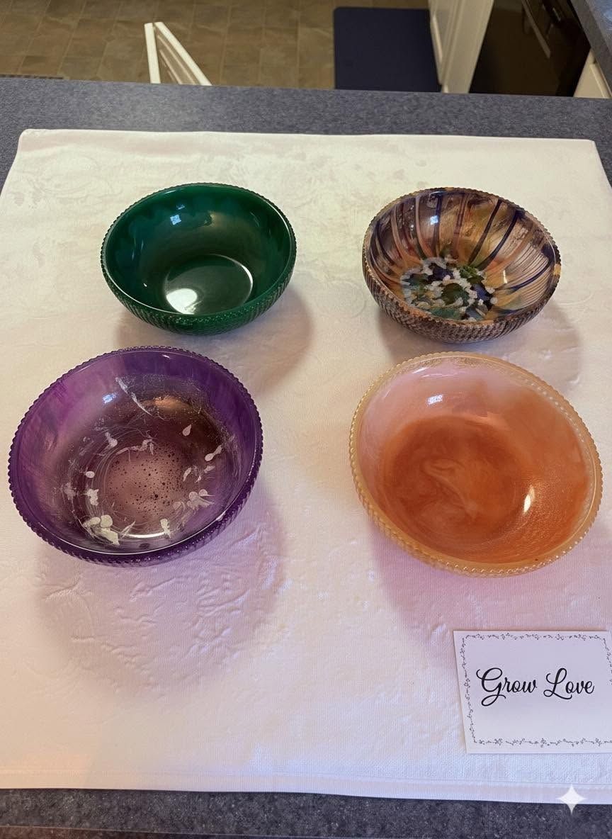 Four small colorful glass bowls arranged on a light surface: green, multicolor, purple, and orange.
