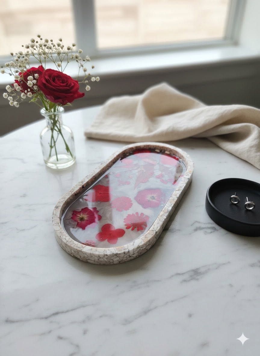 Marble tray with a red floral candle, woven coaster, black lid, and small vase of flowers by a window