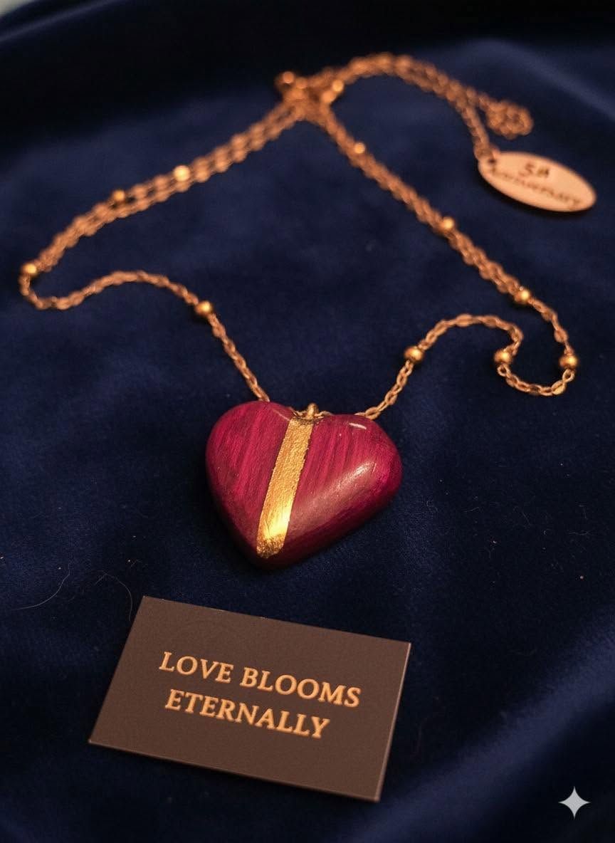 Heart-shaped red pendant necklace on dark fabric with a “LOVE BLOOMS ETERNALLY” tag