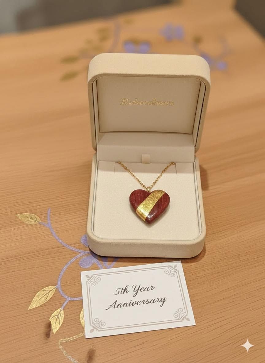 Heart-shaped gold necklace in a gift box with a card reading “To My Anniversary” on a wooden table.