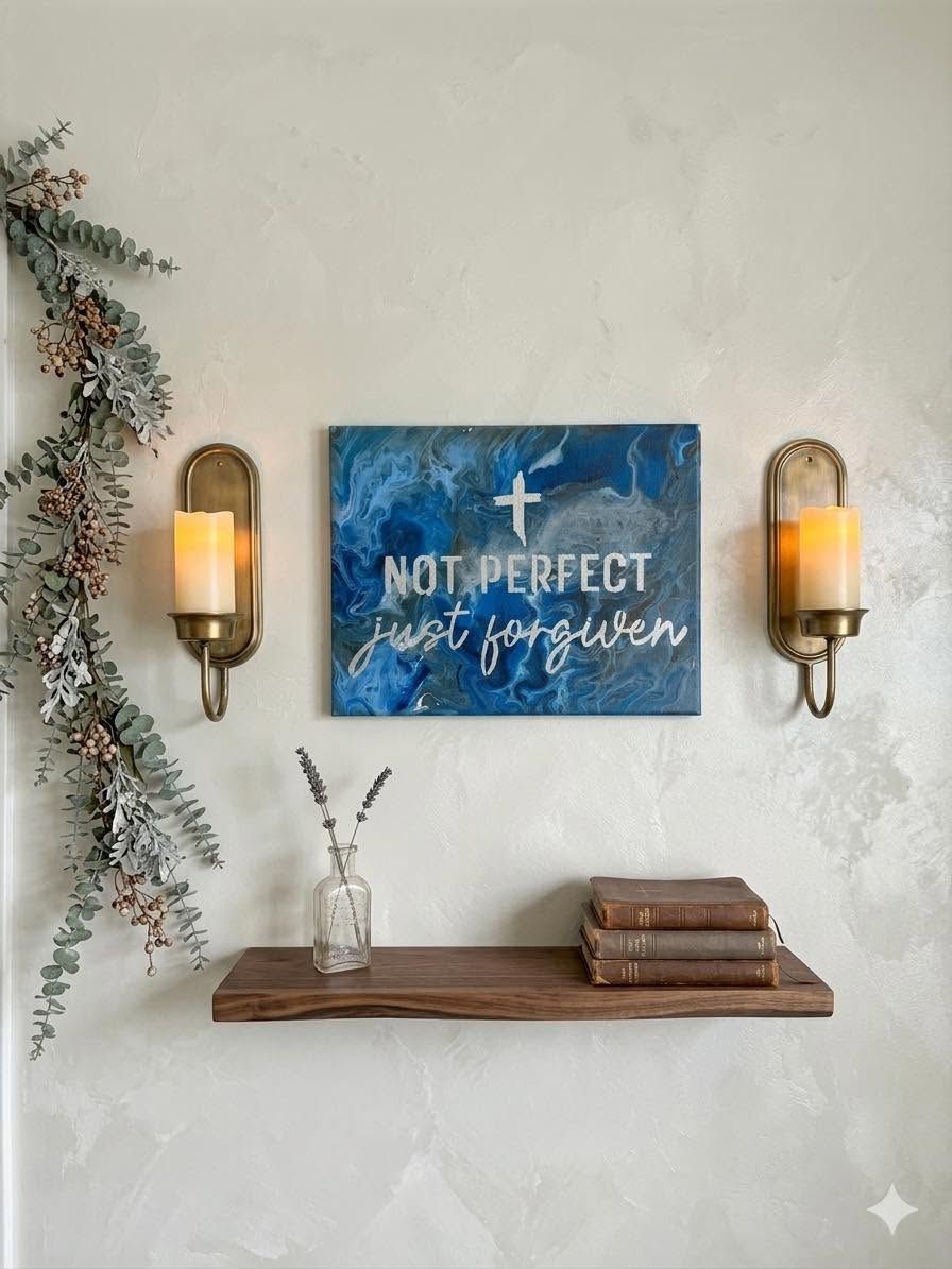 Wall decor with blue “Not Perfect, Just Forgiven” sign, two wall sconces, and a wooden shelf with books and vase.