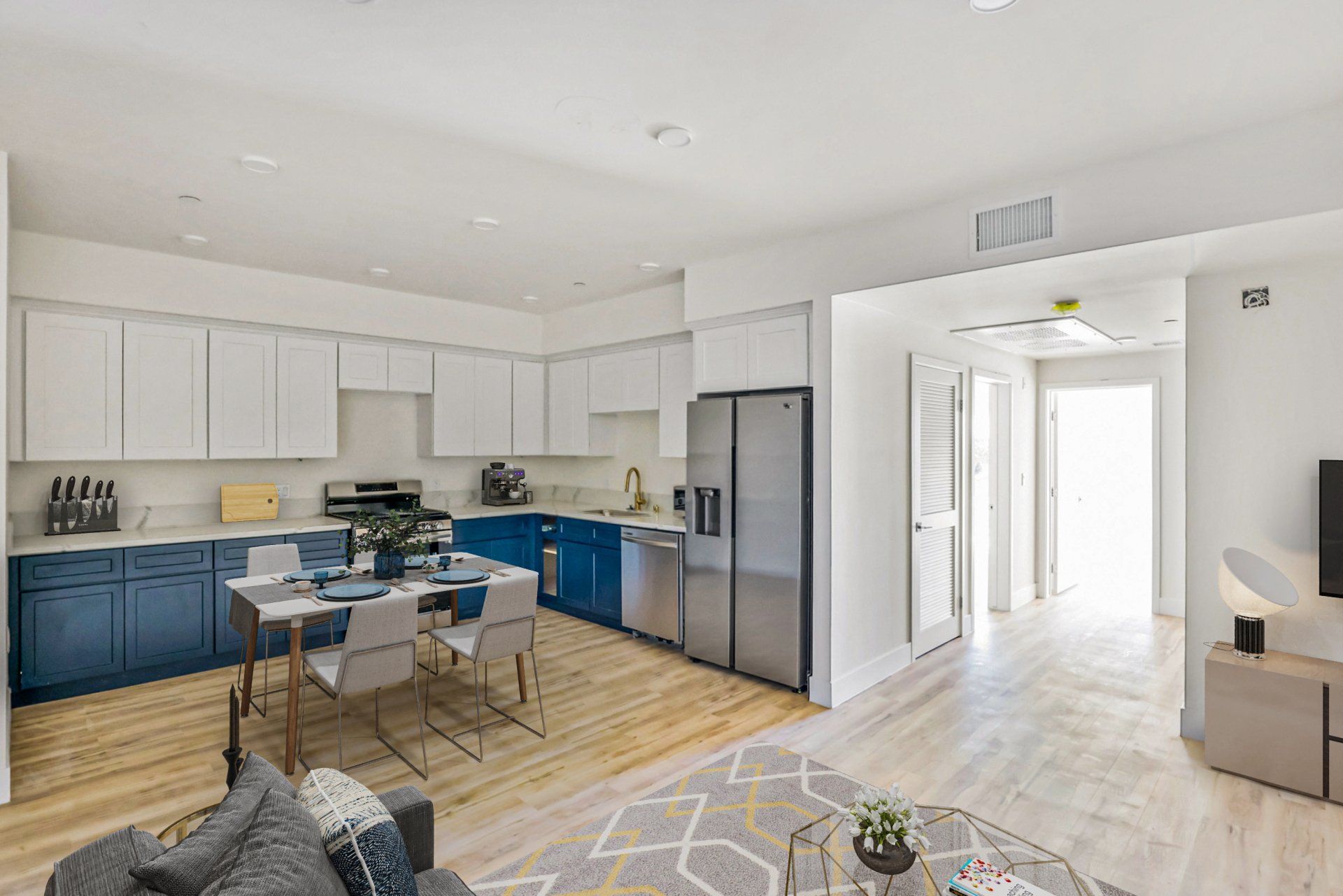 A living room with a couch , table and chairs and a kitchen with blue cabinets and stainless steel appliances.