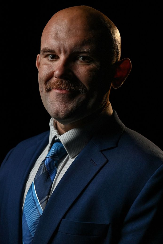 Picture of the founder, Chris Rice. He is a white man that is bald and has a mustache. He is dressed in a navy suit with a white shirt and blue tie. 