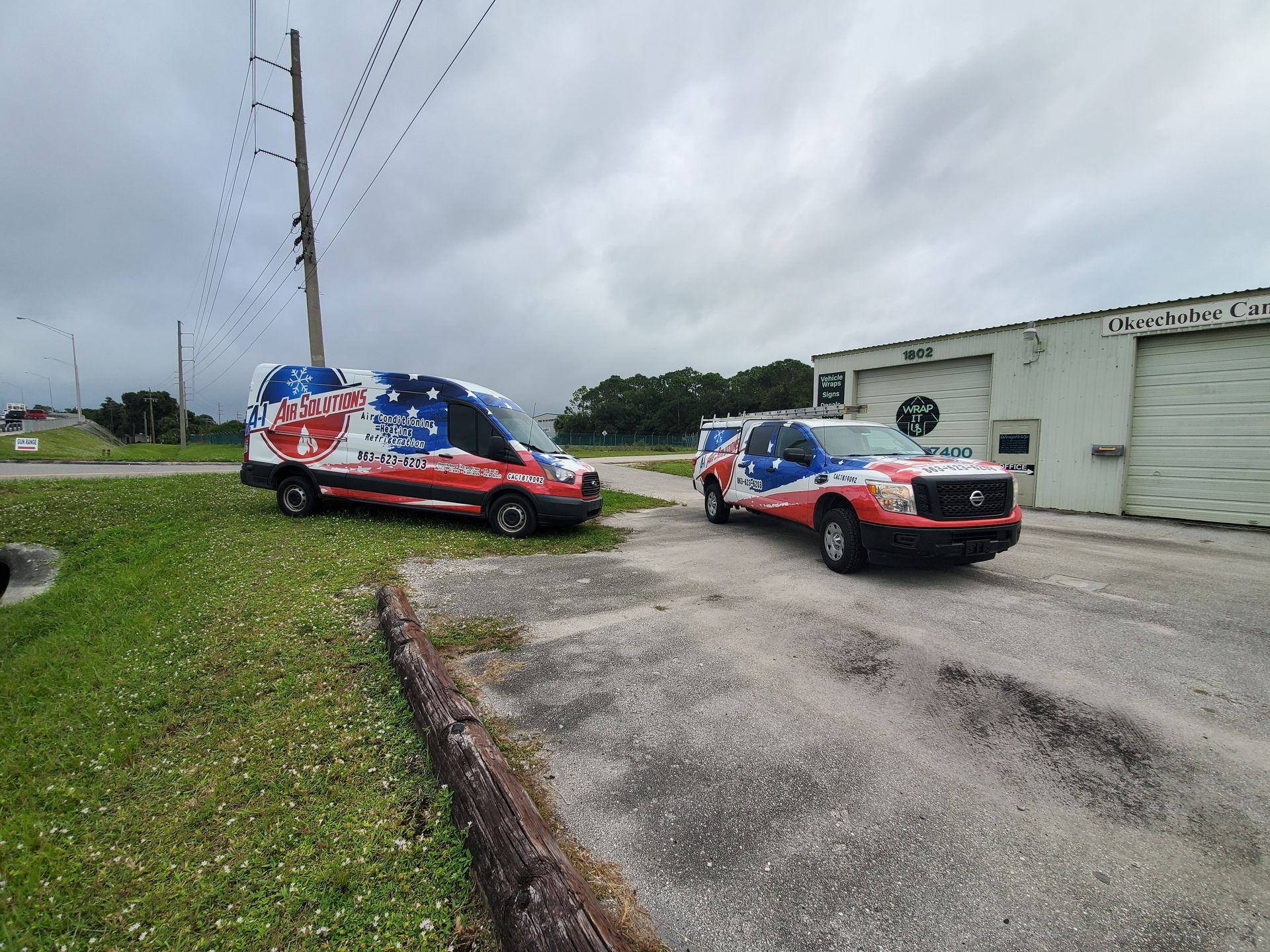 Two vehicles with patriotic-themed wraps parked outside a building on a cloudy day.