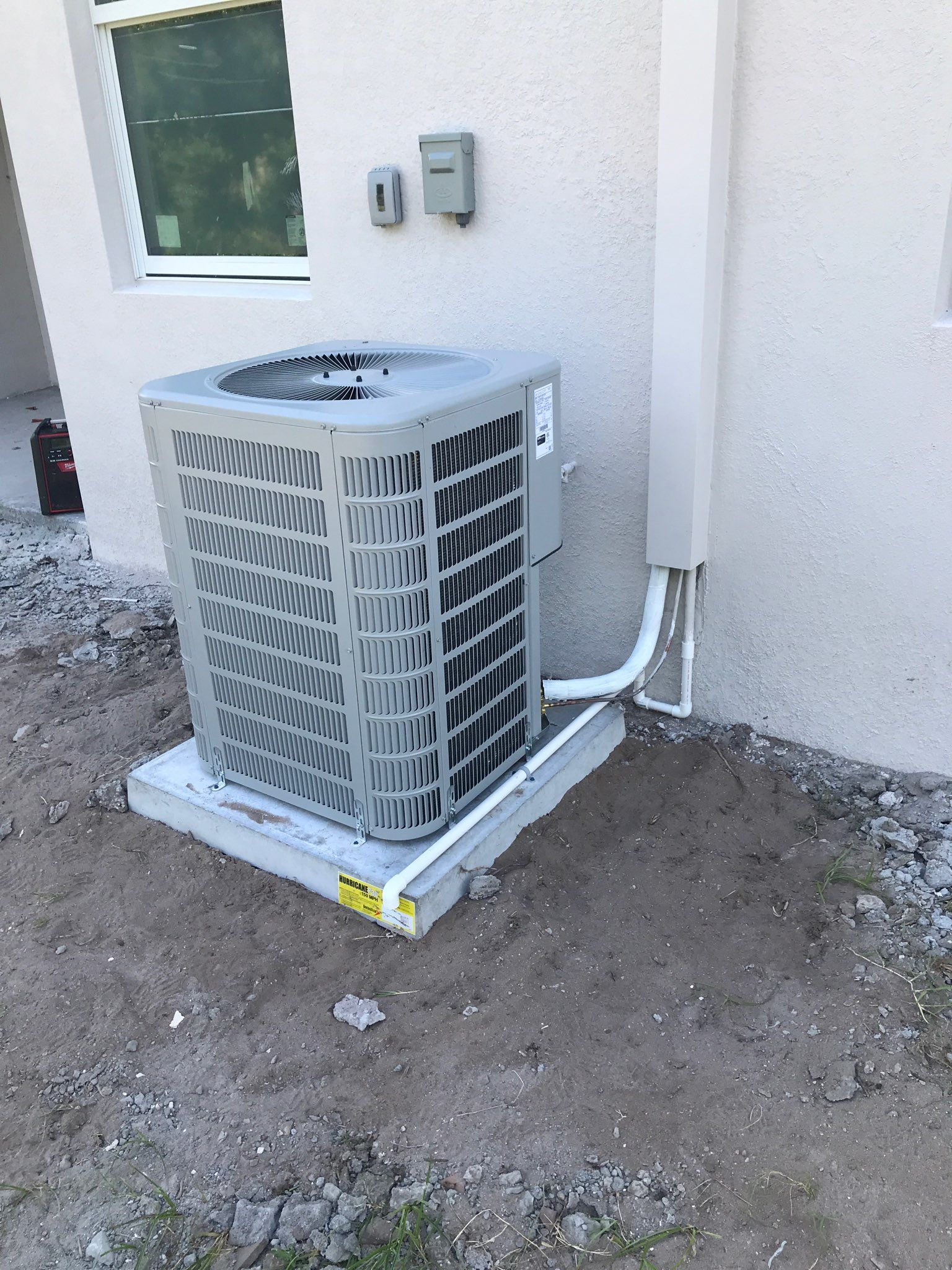 AC unit on a concrete pad next to a white wall, with electrical connections.