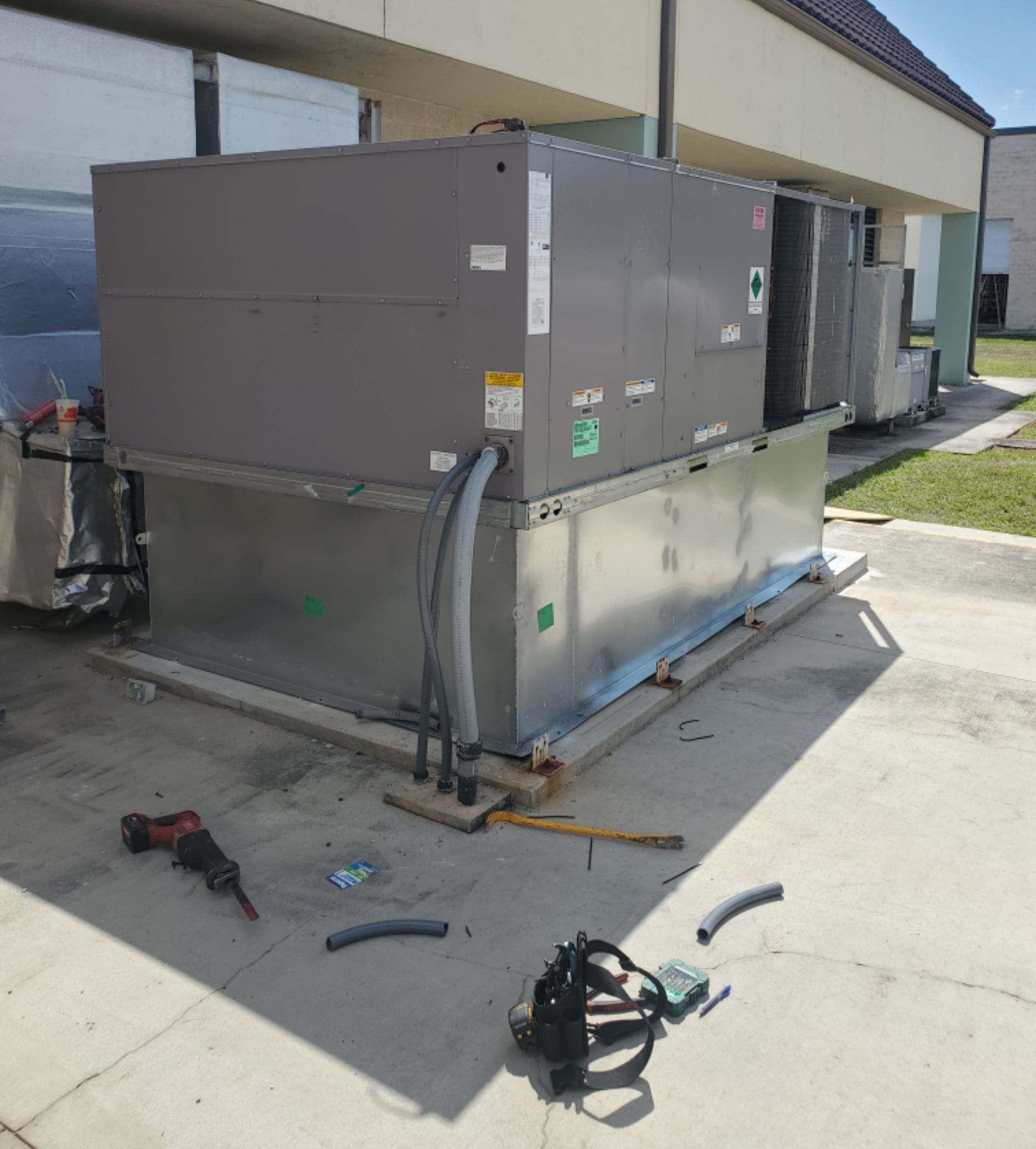 Large HVAC unit outside a building, surrounded by tools and equipment on concrete.