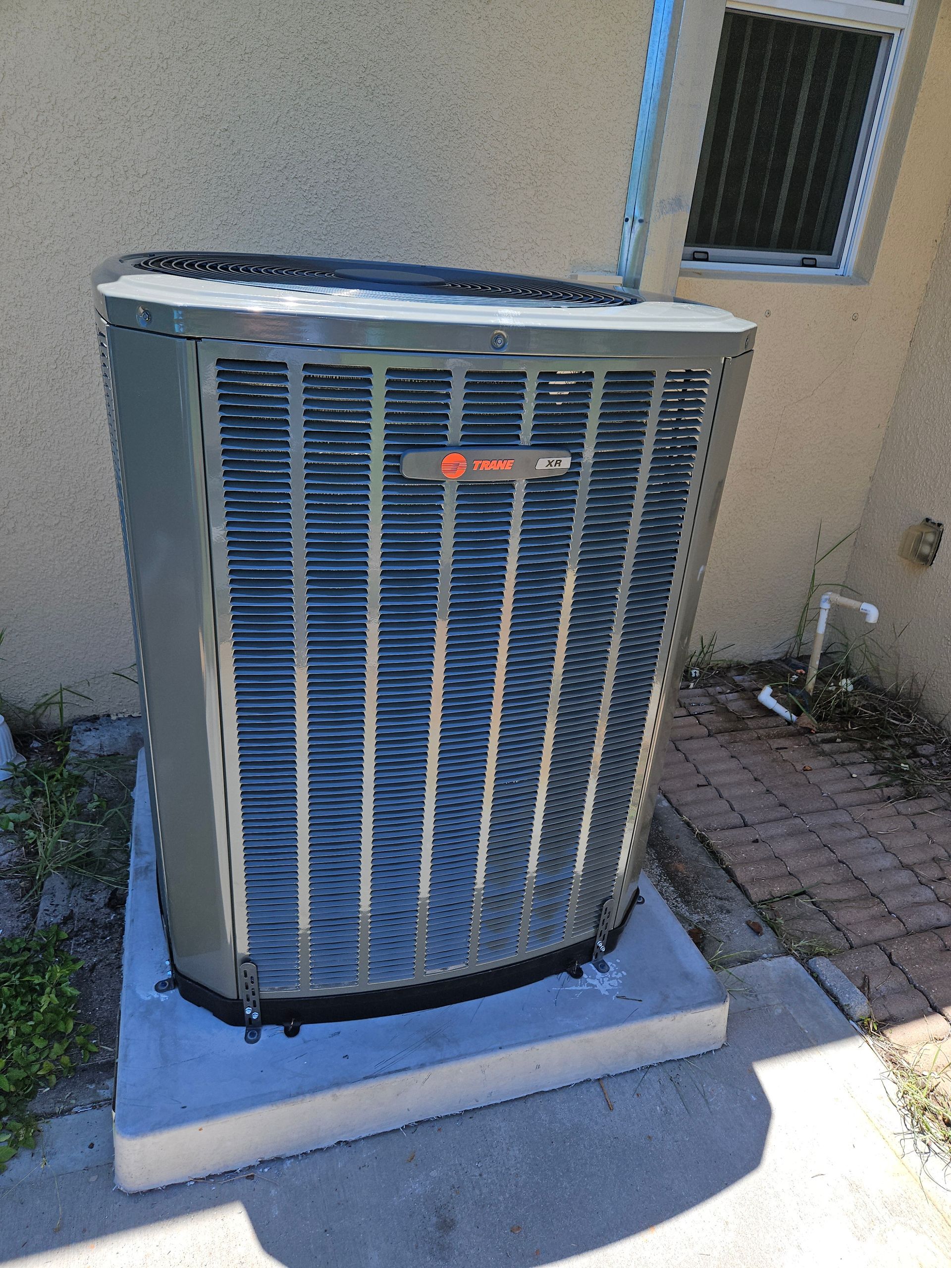 Air conditioning unit, Trane brand, sitting on a concrete pad next to a wall.