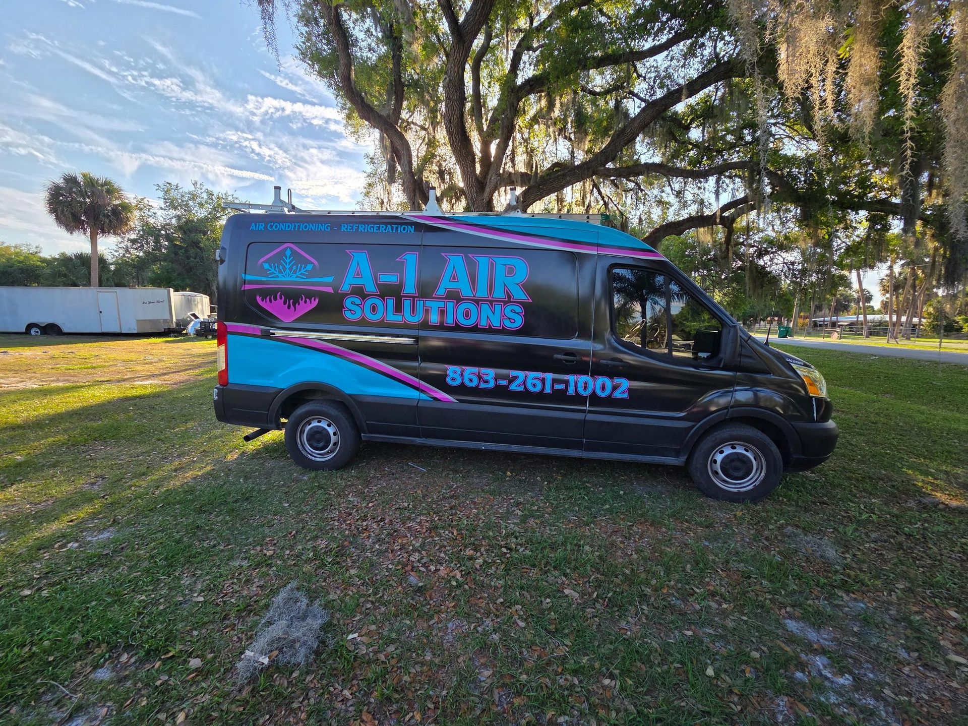 Black and blue A1 Air Solutions van parked on grass under trees, with company logo and phone number.