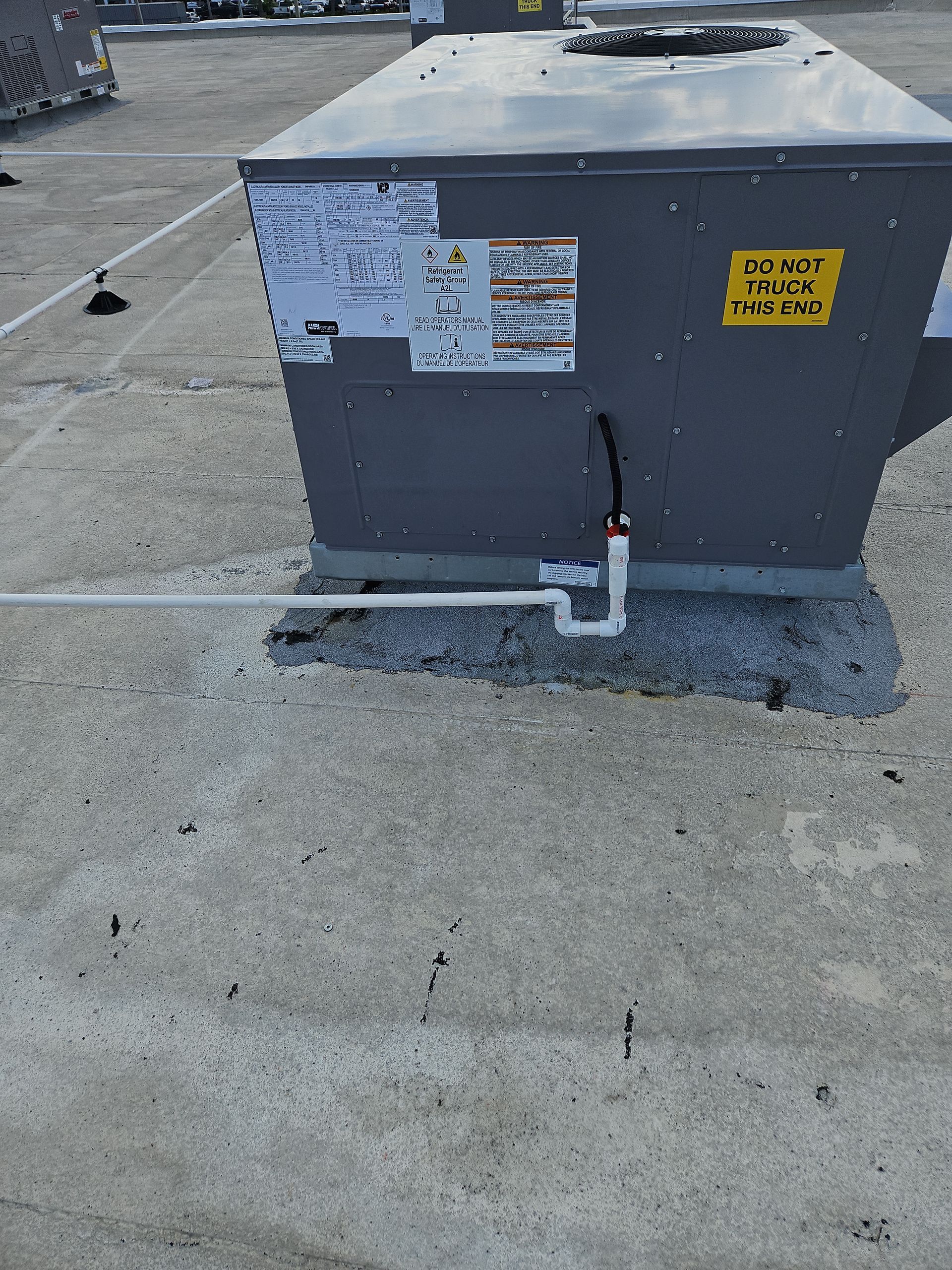 Rooftop HVAC unit with a white drain pipe, on a concrete surface.