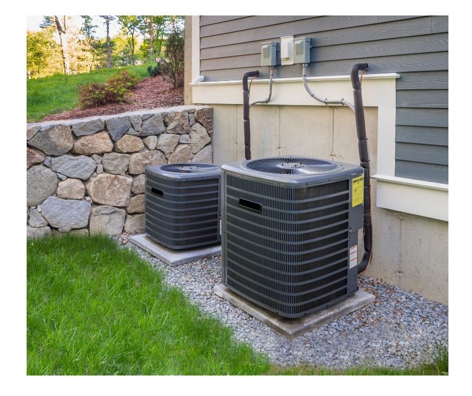Two air conditioning units on concrete pads next to a stone wall and house.
