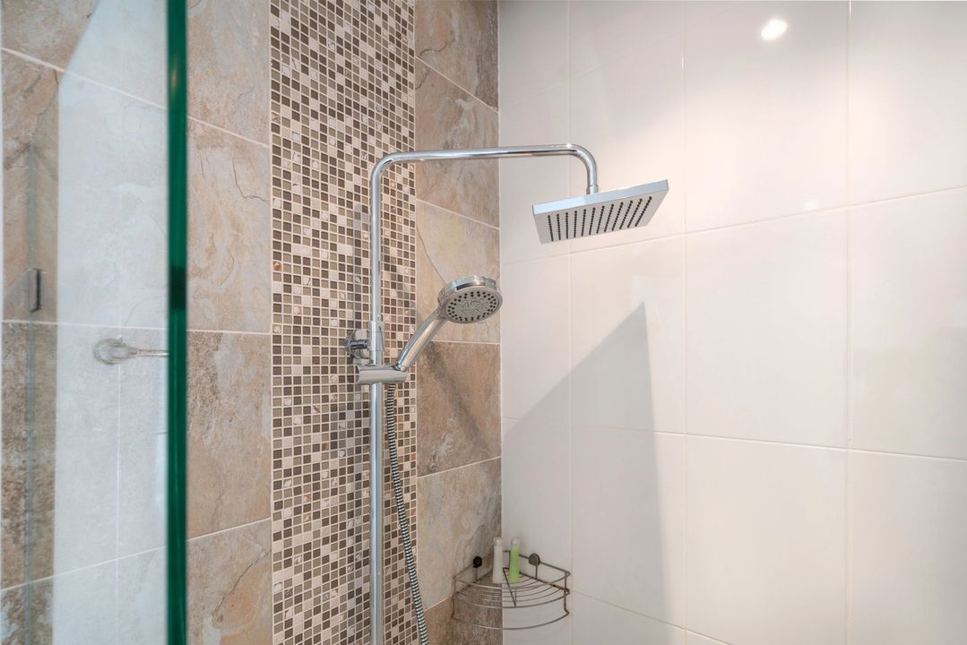 Doccia moderna con porta in vetro, soffione cromato e parete decorativa con piastrelle a mosaico.