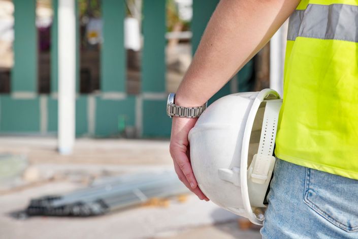 Operaio edile con elmetto bianco in un cantiere, che indossa un giubbotto di sicurezza fluorescente.