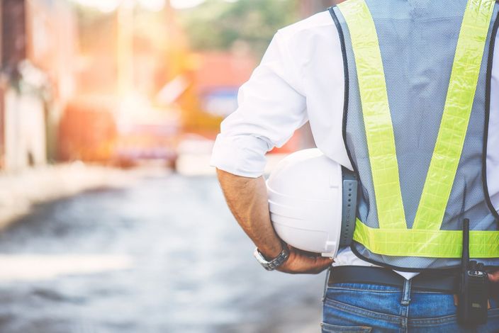Operaio edile con giubbotto riflettente e casco protettivo in un cantiere a bordo strada.