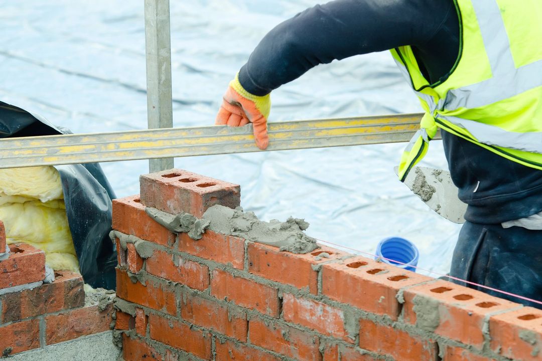Operaio edile che posa mattoni su un muro all'aperto con livella e malta.