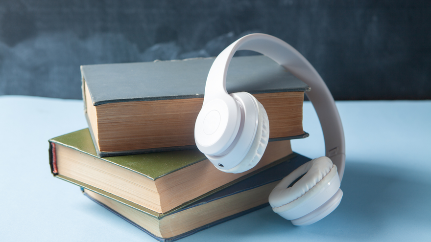 Books stacked with white headphones, on blue surface, against a dark background.
