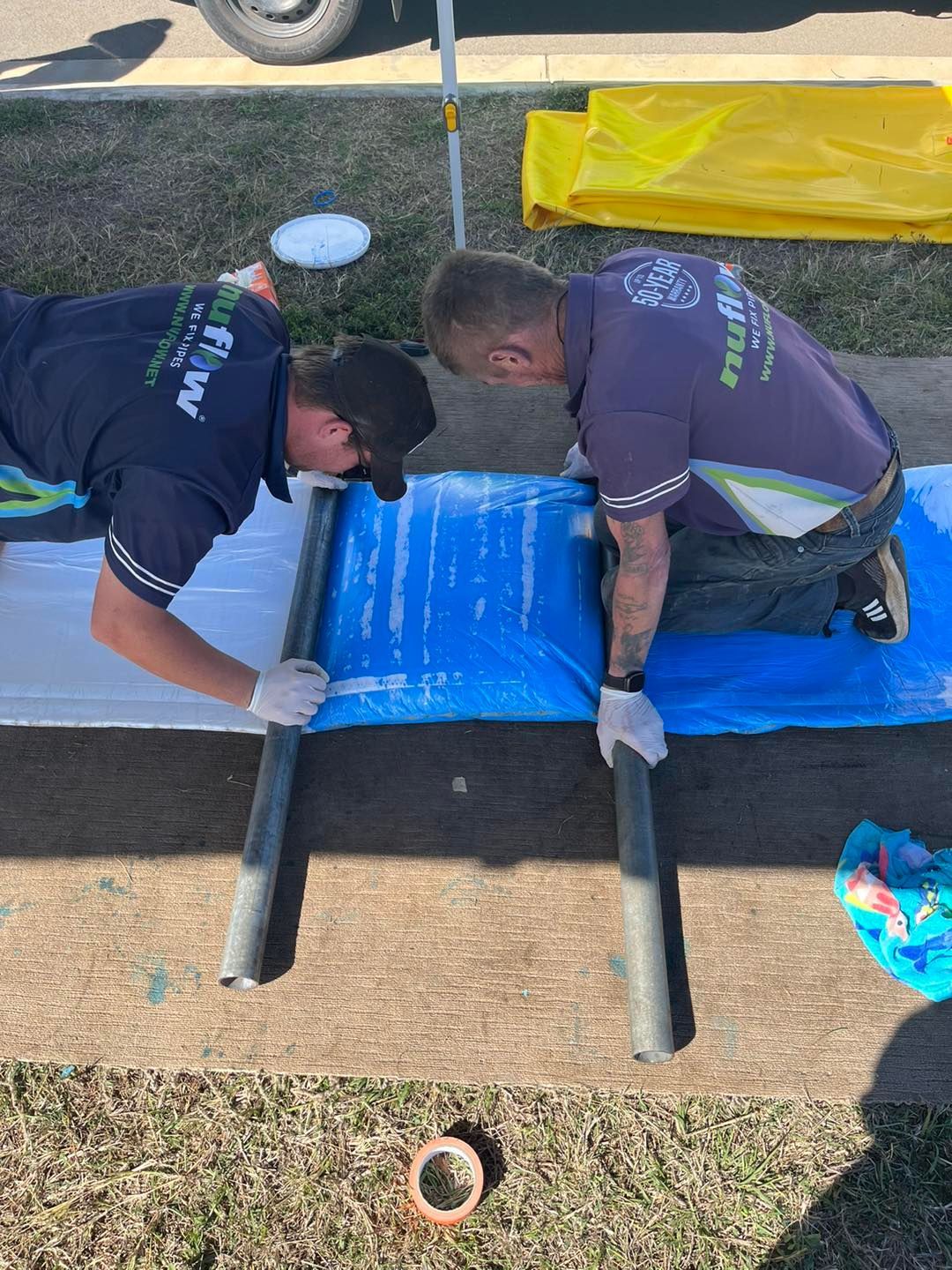 Two men in work shirts install a blue fabric liner, outside on grass. — Nuflow Wide Bay in 1770, QLD